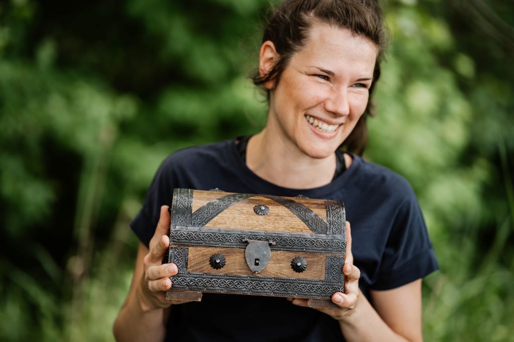 Julia Bauschke lacht und hält eine kleine Schatzkiste